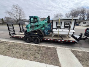 Unique Movers skid loader and small chicken coop on a trailer