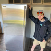 A professional mover posing with a refrigerator he has moved.