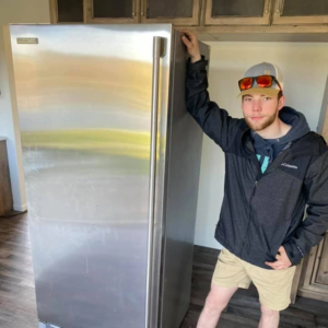 A professional mover posing with a refrigerator he has moved.
