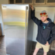 A professional mover posing with a refrigerator he has moved.