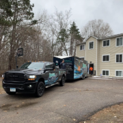 A moving truck and trailer parked outside of an apartment building.