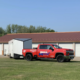 A red Unique Movers moving truck with a white moving trailer parked outside a storage unit.