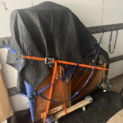 A piano wrapped up and strapped in on a moving trailer.